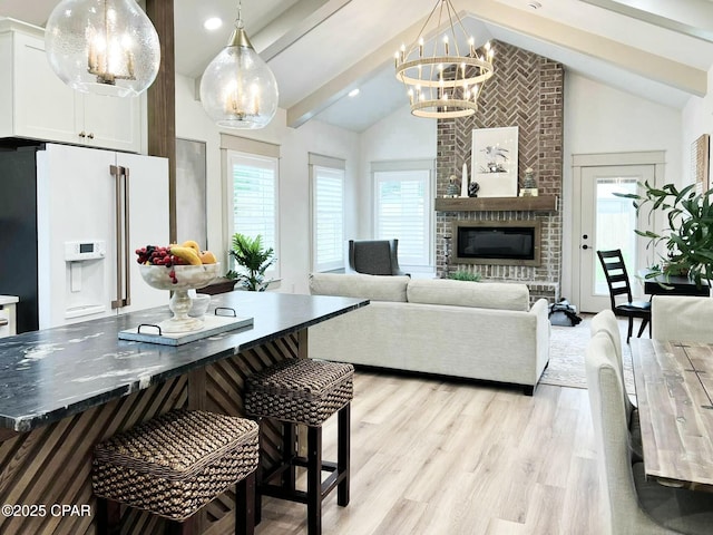 living area with beamed ceiling, light wood-style flooring, a fireplace, an inviting chandelier, and high vaulted ceiling