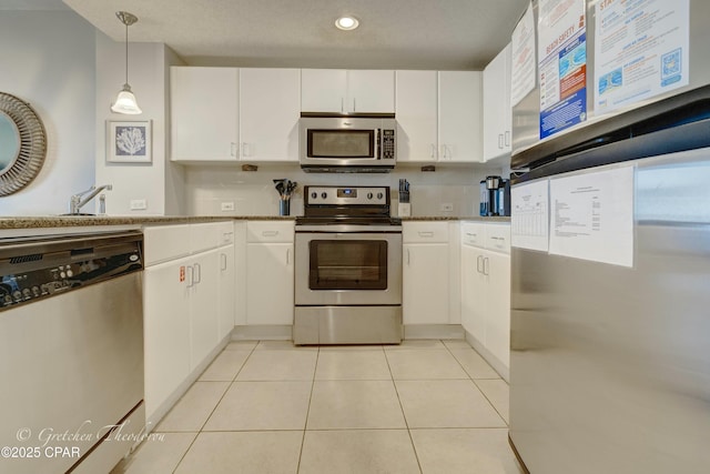 kitchen featuring backsplash, stainless steel appliances, white cabinets, light tile patterned floors, and hanging light fixtures