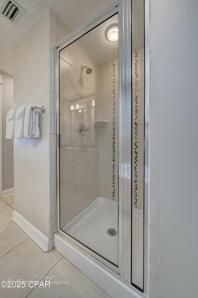 full bath with tile patterned floors, visible vents, a textured ceiling, a shower stall, and baseboards