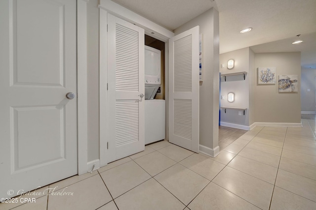 laundry area with light tile patterned floors, baseboards, stacked washer and dryer, and laundry area