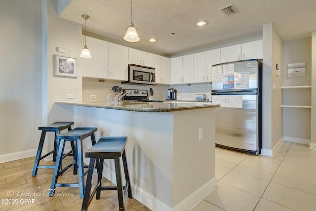 kitchen with visible vents, a peninsula, stainless steel appliances, decorative backsplash, and a kitchen bar