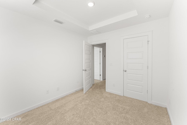 unfurnished bedroom with a tray ceiling, light colored carpet, visible vents, and baseboards