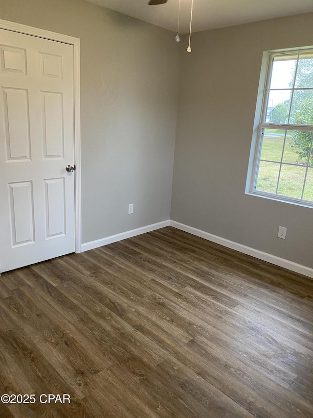 spare room with baseboards, dark wood-style floors, and a ceiling fan