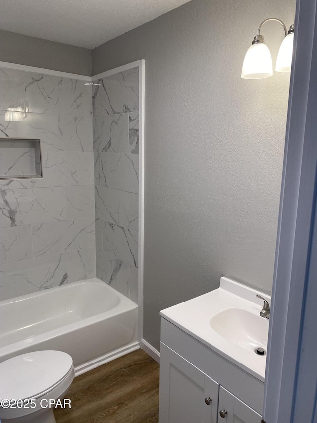 bathroom with toilet, wood finished floors,  shower combination, vanity, and a textured wall