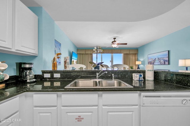 kitchen featuring a ceiling fan, dark stone counters, white dishwasher, a sink, and white cabinetry