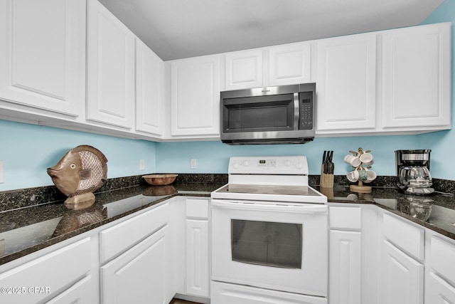 kitchen featuring stainless steel microwave, dark stone counters, white cabinetry, and white electric range