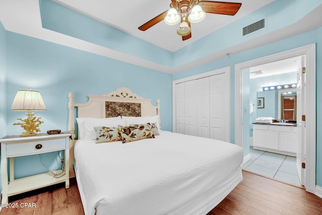 bedroom with a ceiling fan, wood finished floors, visible vents, a closet, and ensuite bathroom