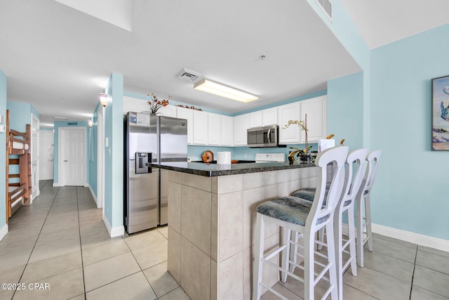 kitchen featuring visible vents, light tile patterned floors, a peninsula, white cabinets, and stainless steel appliances