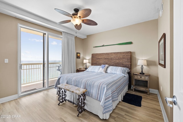 bedroom with wood finished floors, a water view, baseboards, and access to outside