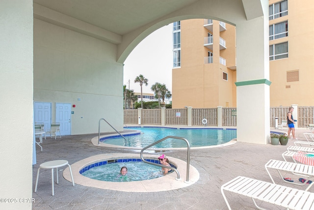 community pool with a hot tub, a patio, and fence