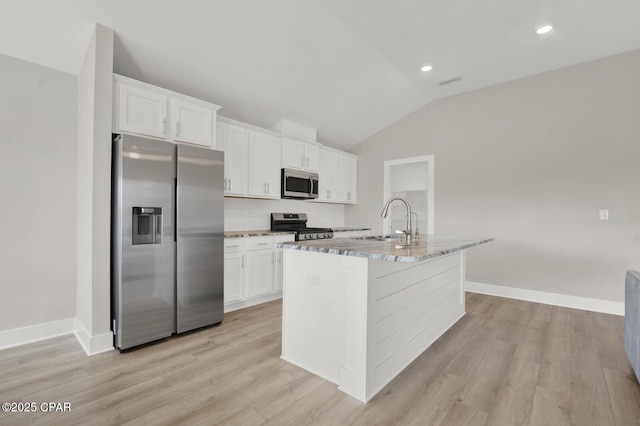 8470 Sun Point Dr, Panama City, FL 32404 - kitchen featuring appliances with stainless steel finishes, vaulted ceiling, decorative backsplash, white cabinetry, and light stone counters