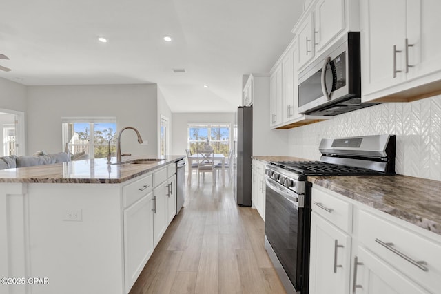 8470 Sun Point Dr, Panama City, FL 32404 - kitchen featuring appliances with stainless steel finishes, stone counters, a kitchen island with sink, backsplash, and white cabinets