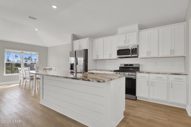 8470 Sun Point Dr, Panama City, FL 32404 - kitchen with stainless steel appliances, vaulted ceiling, a center island with sink, tasteful backsplash, and light stone countertops