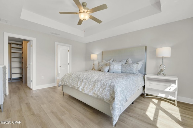 8470 Sun Point Dr, Panama City, FL 32404 - bedroom with a tray ceiling, light wood-style flooring, a walk in closet, a ceiling fan, and ensuite bathroom