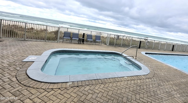 community pool with a patio area, fence, a view of the beach, and a water view