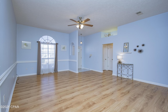 empty room featuring a ceiling fan, arched walkways, visible vents, and light wood finished floors