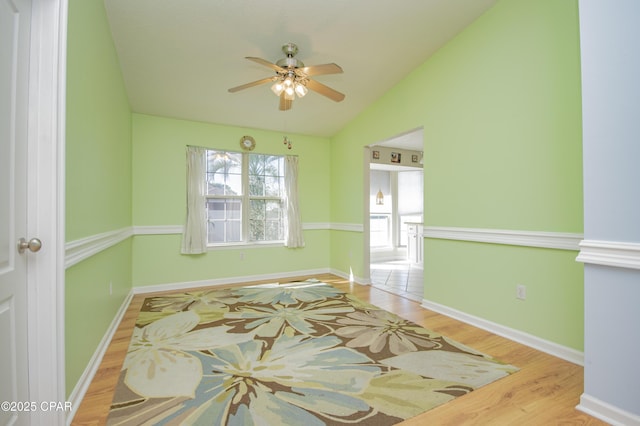 empty room with a ceiling fan, lofted ceiling, wood finished floors, and baseboards