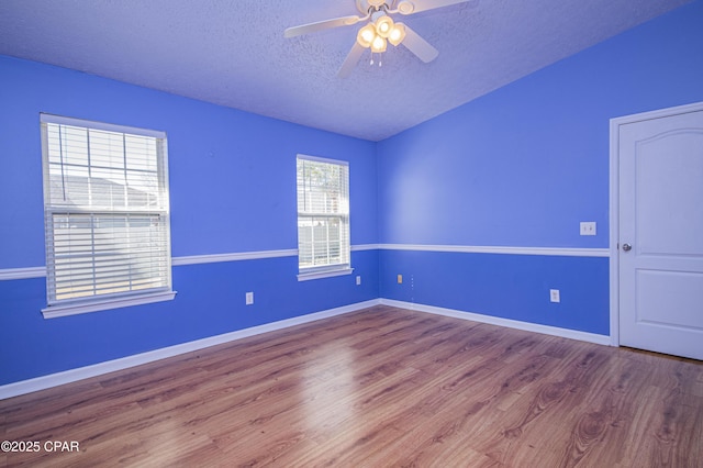 unfurnished room featuring a textured ceiling, wood finished floors, baseboards, ceiling fan, and vaulted ceiling