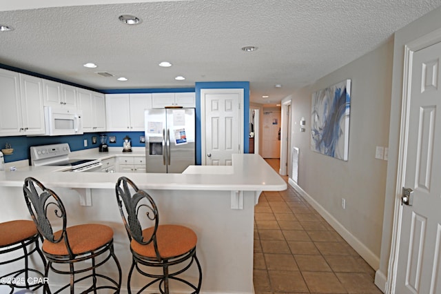 10811 Front Bch Unit 501, Panama City Beach, FL 32407 - kitchen with white appliances, a peninsula, a kitchen bar, light tile patterned flooring, and a textured ceiling