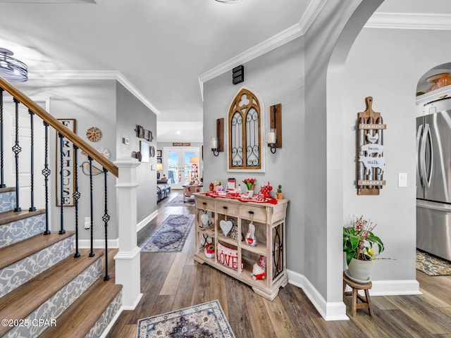 foyer with crown molding, baseboards, stairs, hardwood / wood-style floors, and arched walkways