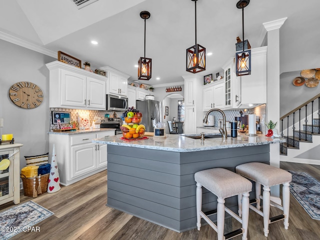 kitchen featuring crown molding, a peninsula, arched walkways, stainless steel appliances, and a sink