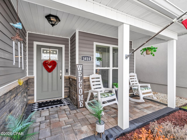 view of exterior entry with stone siding and covered porch