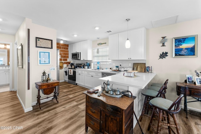 kitchen featuring wood finished floors, a breakfast bar, stainless steel appliances, light countertops, and white cabinetry