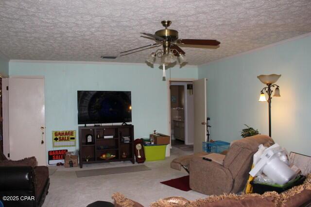 living area with a ceiling fan, visible vents, carpet floors, a textured ceiling, and crown molding