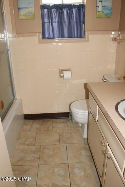 bathroom featuring shower / bath combination with glass door, toilet, tile walls, and vanity