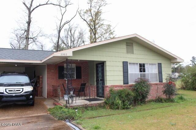 ranch-style house featuring a front lawn, brick siding, a porch, and a carport