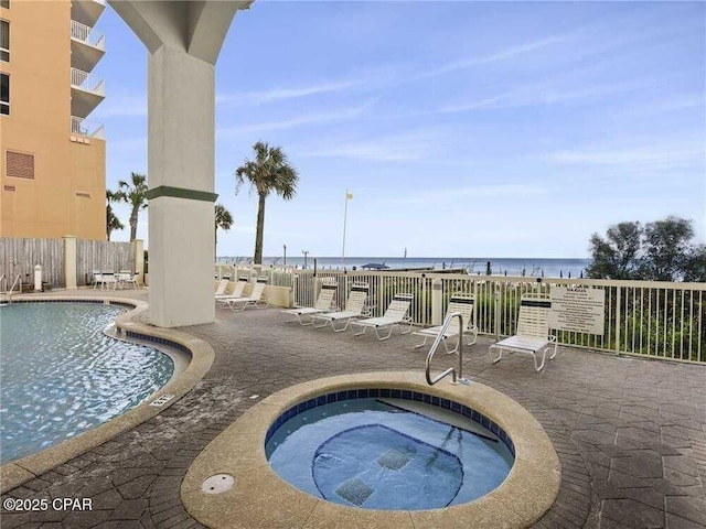 pool featuring a patio, fence, a community hot tub, and a water view