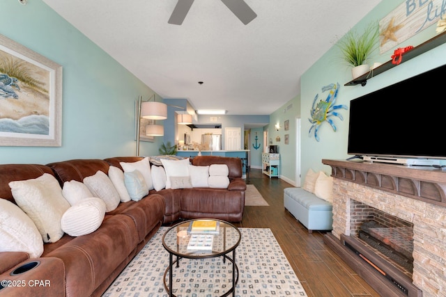 living area with a stone fireplace, baseboards, a ceiling fan, and dark wood-style flooring