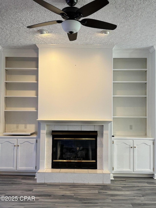 interior details with wood finished floors, a tile fireplace, a textured ceiling, and ornamental molding