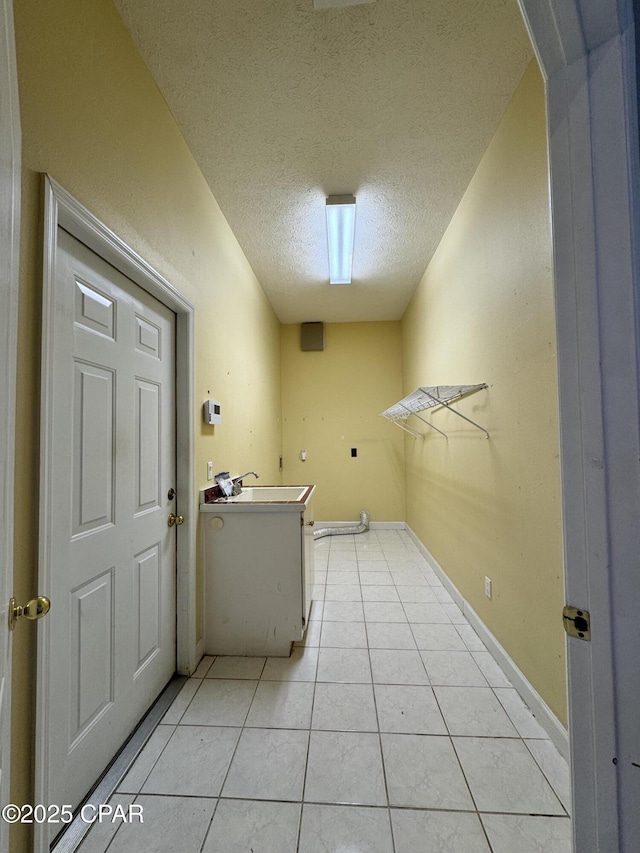 laundry room with light tile patterned floors, baseboards, a textured ceiling, and a sink