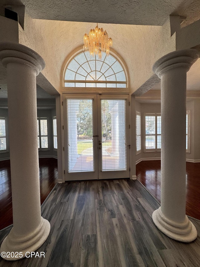 entrance foyer with dark wood finished floors, french doors, decorative columns, a chandelier, and a textured wall