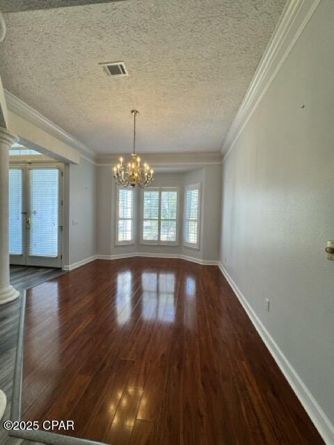 unfurnished room with a notable chandelier, a textured ceiling, wood finished floors, crown molding, and decorative columns