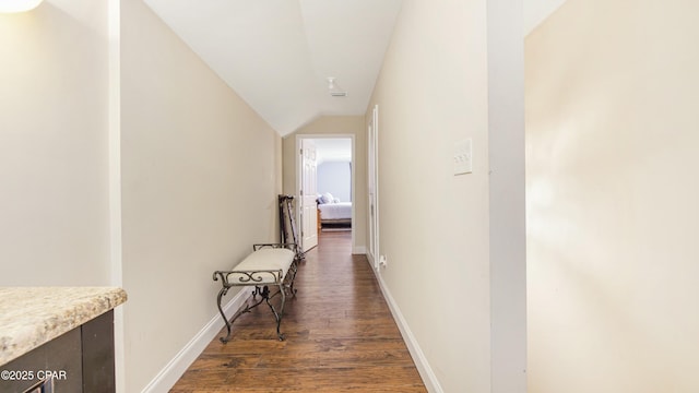 corridor featuring lofted ceiling, wood finished floors, and baseboards