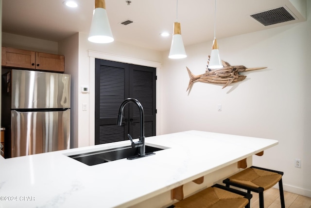 kitchen with decorative light fixtures, a sink, visible vents, and freestanding refrigerator