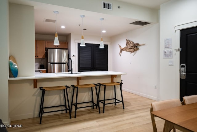 kitchen with a peninsula, a sink, visible vents, freestanding refrigerator, and a kitchen bar