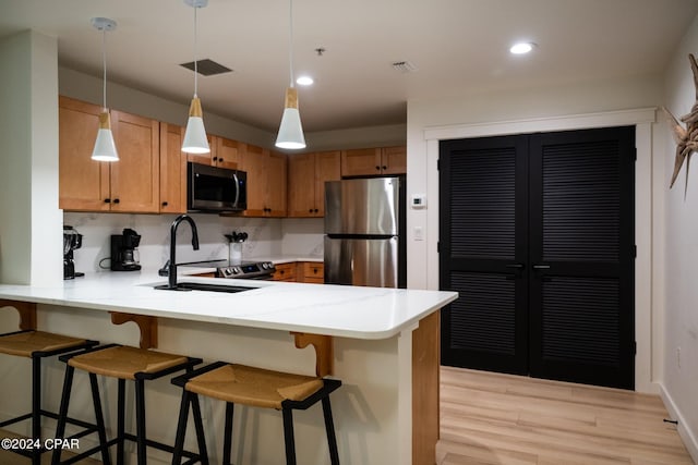 kitchen with light wood finished floors, stainless steel appliances, a peninsula, a sink, and visible vents
