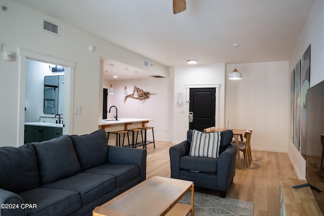 living room featuring light wood-type flooring, baseboards, visible vents, and ceiling fan