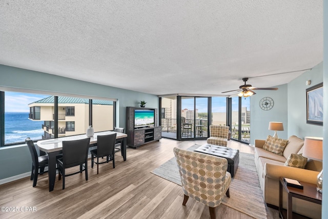 living area featuring wood finished floors, baseboards, ceiling fan, floor to ceiling windows, and a textured ceiling