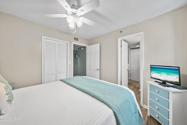 bedroom with baseboards, visible vents, dark wood finished floors, ceiling fan, and a closet