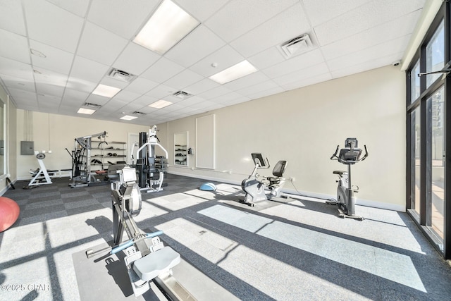 exercise room featuring visible vents, a paneled ceiling, and baseboards