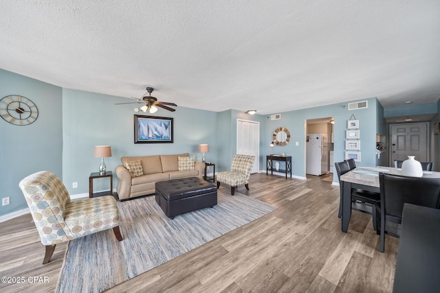 living area with baseboards, wood finished floors, visible vents, and a textured ceiling