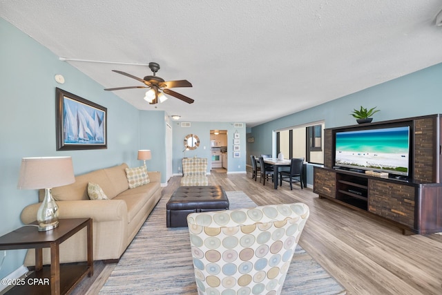 living area with a ceiling fan, wood finished floors, baseboards, and a textured ceiling