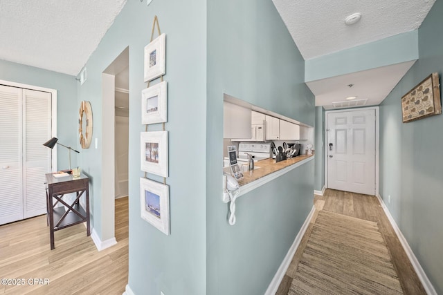 hallway featuring baseboards, light wood-type flooring, and a textured ceiling