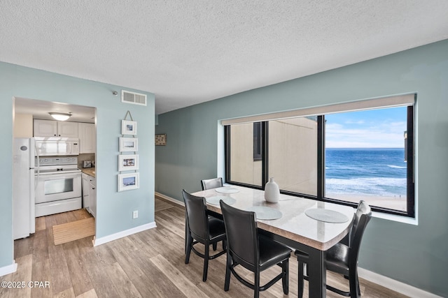 dining area featuring baseboards, visible vents, light wood finished floors, and a textured ceiling