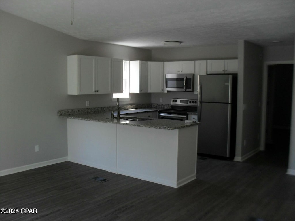 kitchen with a sink, a peninsula, white cabinetry, and stainless steel appliances