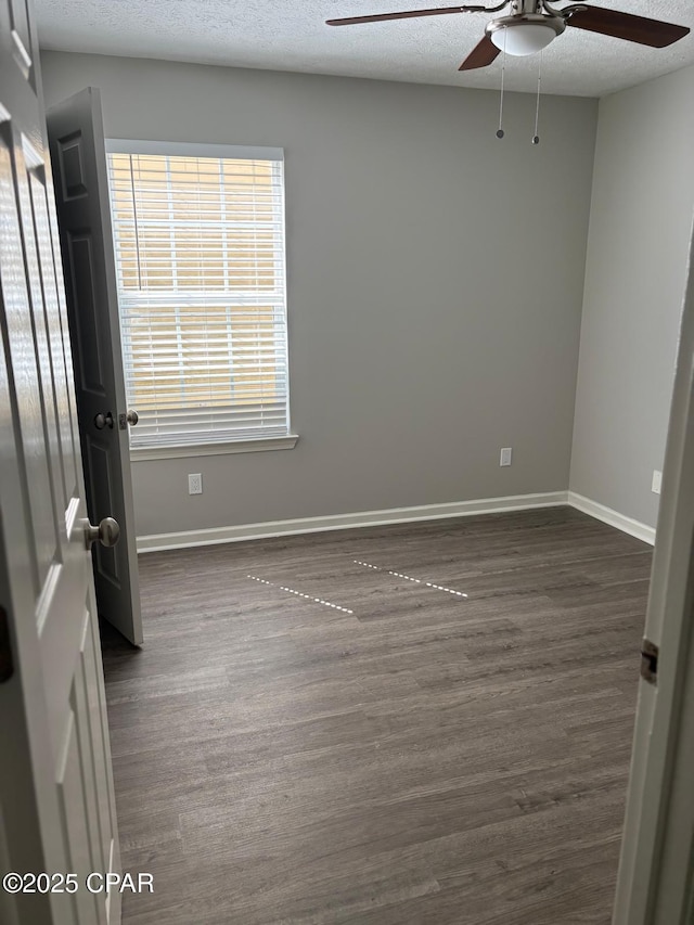 empty room featuring ceiling fan, dark wood-style flooring, and baseboards